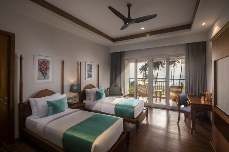 Ein elegantes Twin-Zimmer im Amal Tamara Resort mit Balkon und Blick auf Palmen und Meer.