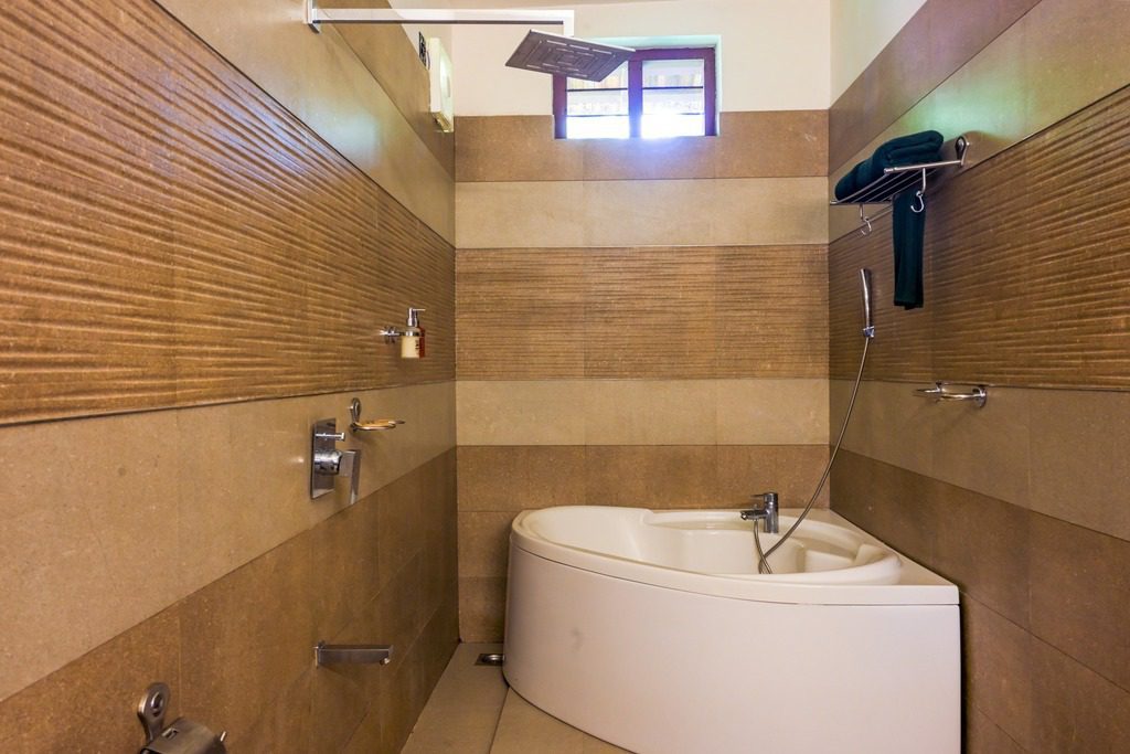 Die Ayur Villa im Ayur On The Beach Nattika bietet ein elegantes Badezimmer mit Eckbadewanne und Regendusche.