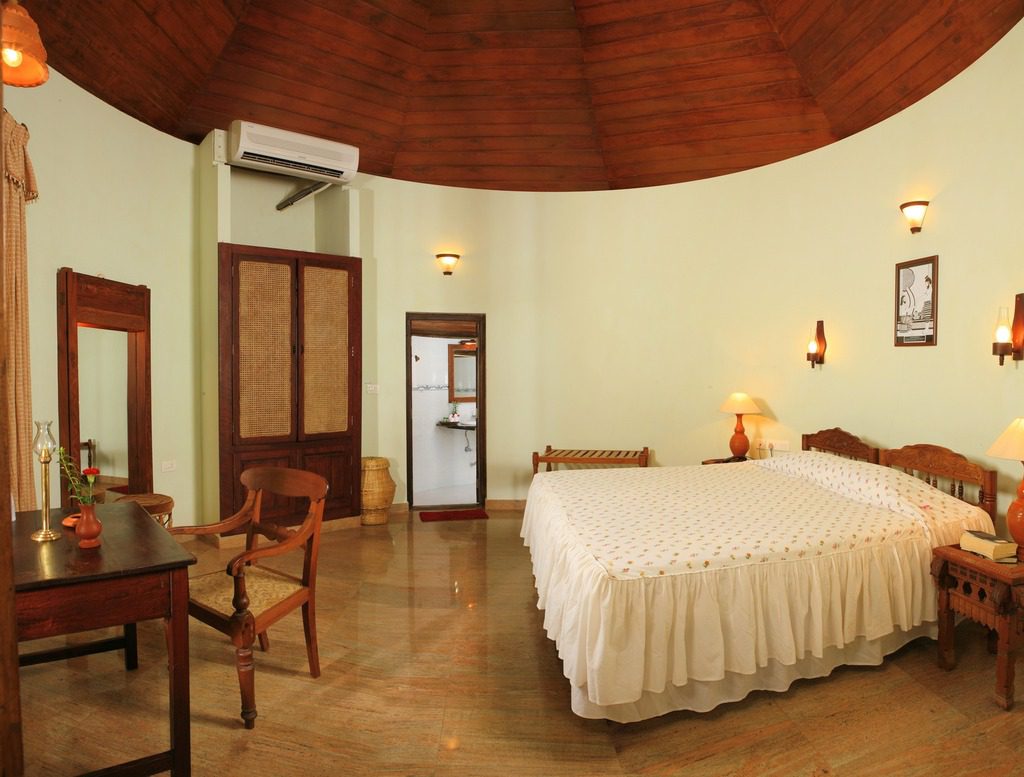 Ein geräumiges Deluxe-Zimmer im Manaltheeram Ayurveda Beach Village mit traditioneller Kerala-Einrichtung und rundem Holzdecke.