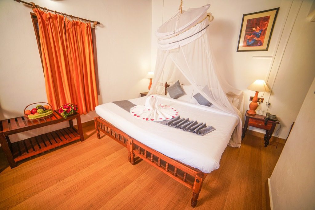 Ein liebevoll hergerichtetes Standardzimmer im Manaltheeram Ayurveda Beach Village mit Baldachinbett und Blumendekoration.
